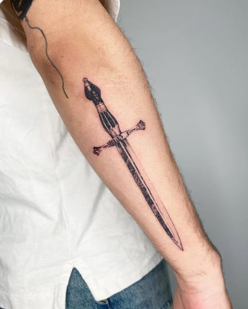 A black and grey linework tattoo of a dagger on the forearm, featuring clean lines and minimal shading — by Level tattoo, los angeles