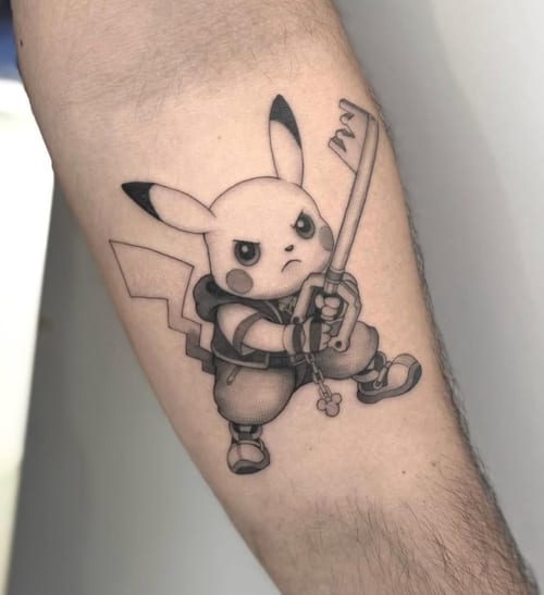 A black and grey tattoo of Pikachu holding a sword on the forearm, featuring bold outlines and a cartoonish style — by otaybeatdown, los angeles