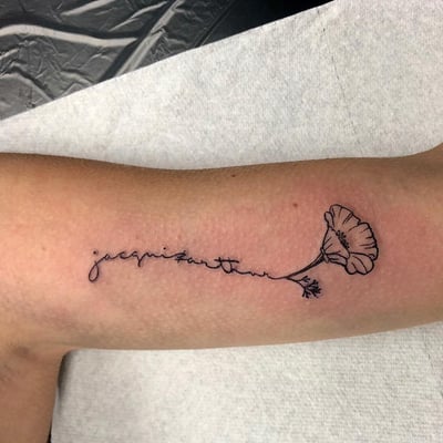 A delicate fine line tattoo of a flower with script on the forearm, done in black ink — by Sandra Price, los angeles
