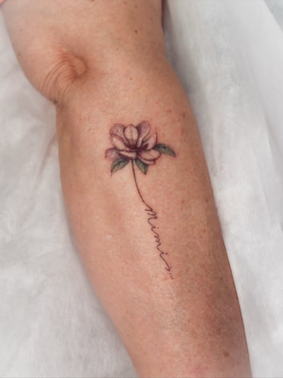 A delicate fine line flower tattoo with script on the forearm, featuring a minimalist design in color — by Melanie Benoit, los angeles