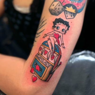 A colorful tattoo of Betty Boop sitting on a slot machine with hearts, done in a neo-traditional style on the arm — by Maddie Ramirez, los angeles