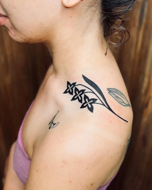 A minimalist blackwork floral design on the shoulder, featuring delicate flowers and leaves — by Dylan Aiello, los angeles