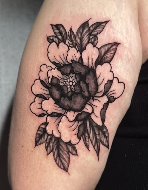 A black and grey floral tattoo on the upper arm featuring a large, detailed flower with leaves in a bold blackwork style — by Shelby Bianco, los angeles