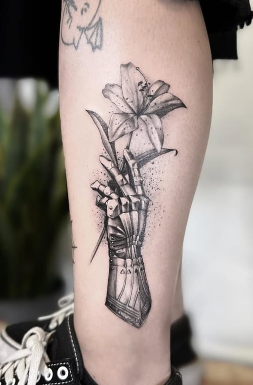 A black and grey illustrative tattoo of a mechanical hand holding a flower on the calf, featuring detailed linework and dot shading — by Jian Liang, los angeles