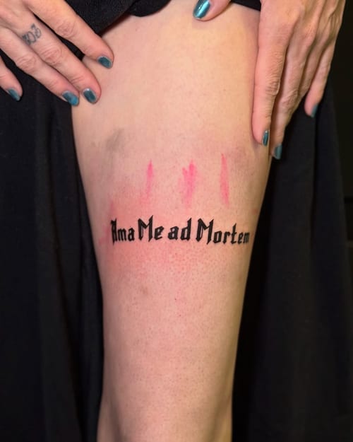 A bold black script lettering tattoo on the thigh featuring a Latin phrase — by zealous, los angeles