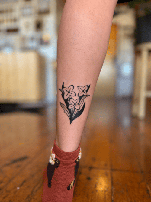 A minimalist blackwork tattoo of three flowers on the calf, featuring simple lines and solid black shading — by Dylan Aiello, los angeles