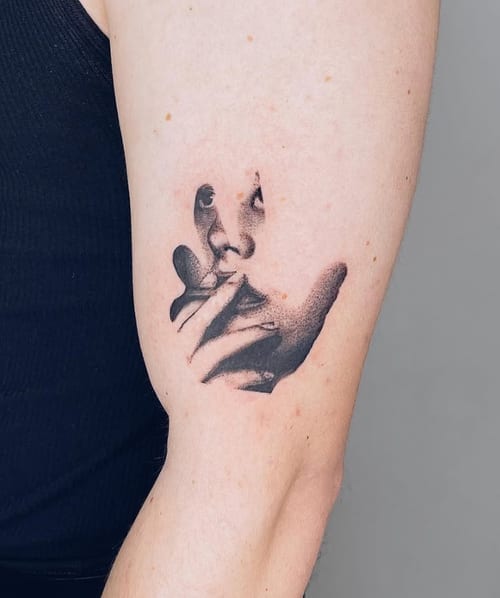 A surreal blackwork tattoo of a face on the upper arm, featuring abstract and distorted elements with strong contrast — by Level tattoo, los angeles