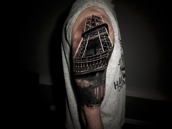 A detailed black and grey realism tattoo of the Eiffel Tower on the upper arm, showcasing intricate architectural details — by Travis Ross, inglewood, ca