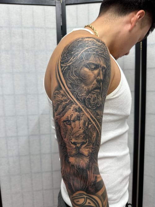 A detailed black and grey realism tattoo of Jesus Christ and a lion on a full sleeve, showcasing intricate shading and texture — by Humilde tattoos, los angeles