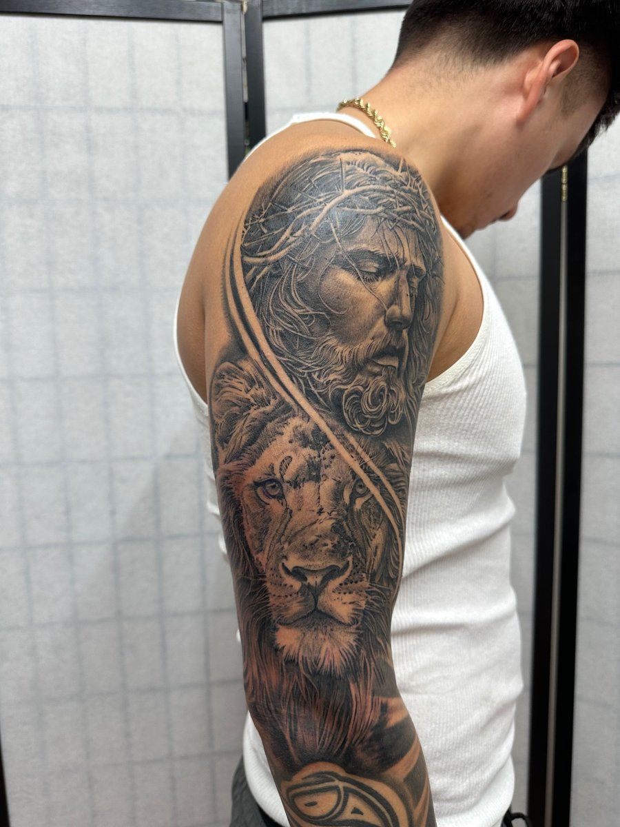 A detailed black and grey realism tattoo of Jesus Christ and a lion on a full sleeve, showcasing intricate shading and texture — by Humilde tattoos, los angeles