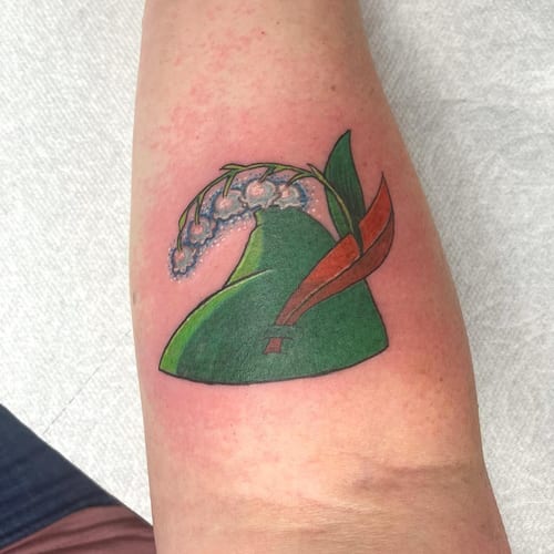 A colorful tattoo of a green hat with flowers on the forearm, done in a bold traditional style — by Sandra Price, los angeles