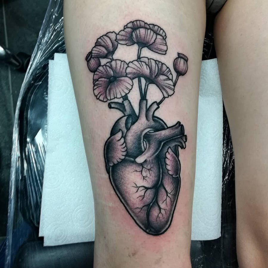 A bold black and grey tattoo of an anatomical heart with flowers on the thigh — by Samuel Connelly, los angeles