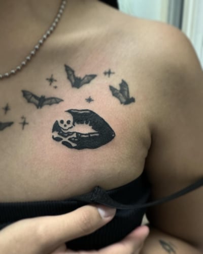 A blackwork tattoo of lips with a skull and bats on the chest — by Maddie Ramirez, los angeles