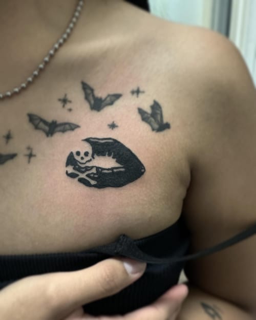 A blackwork tattoo of lips with a skull and bats on the chest — by Maddie Ramirez, los angeles