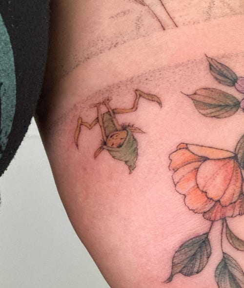 A whimsical tattoo of a small creature with a flower on the arm, done in an illustrative fine line style with delicate colors — by Melanie Benoit, los angeles