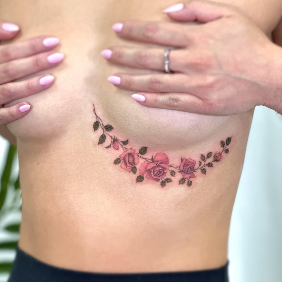 A delicate rose vine tattoo in color on the rib, featuring fine line work and a romantic floral design — by Melanie Benoit, los angeles