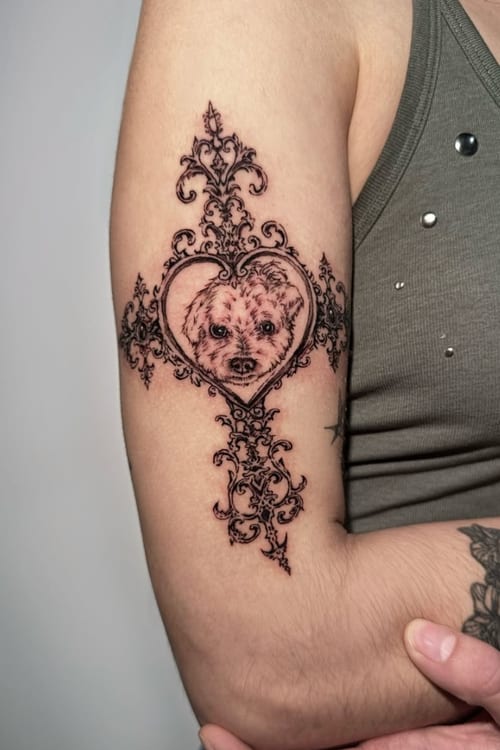 A fine line black and grey tattoo of an animal's face within an ornate heart design on the upper arm — by Shelby Bianco, los angeles