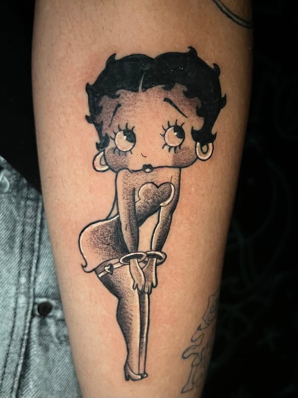 A black and grey illustrative tattoo of a cartoon woman on the forearm, featuring bold outlines and shading — by Josue Bravo, los angeles