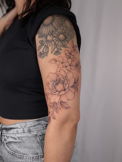 A delicate black and grey floral tattoo on the upper arm featuring a detailed arrangement of flowers — by Melanie Benoit, los angeles