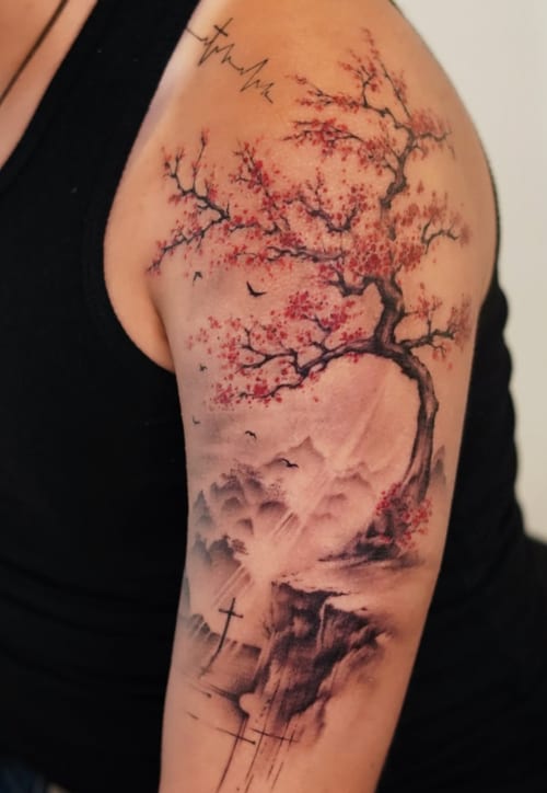 A watercolor and illustrative tattoo on the upper arm depicting a tree with red leaves, a mountainous landscape, and crosses, blending color and black ink — by Jian Liang, los angeles