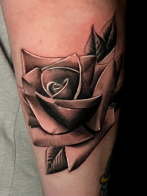A realistic black and grey rose tattoo on the upper arm, showcasing detailed shading and depth — by Josue Bravo, los angeles