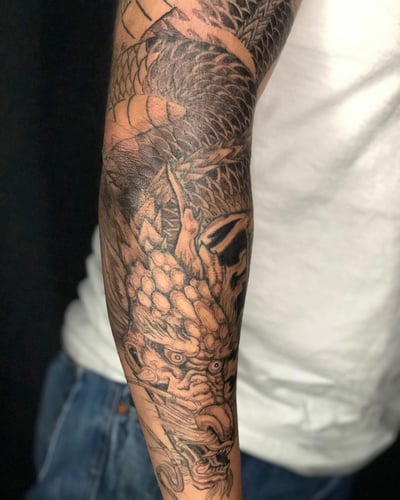 A bold black and grey Japanese dragon tattoo on the arm, featuring intricate scale details and dynamic shading — by Sandra Price, los angeles