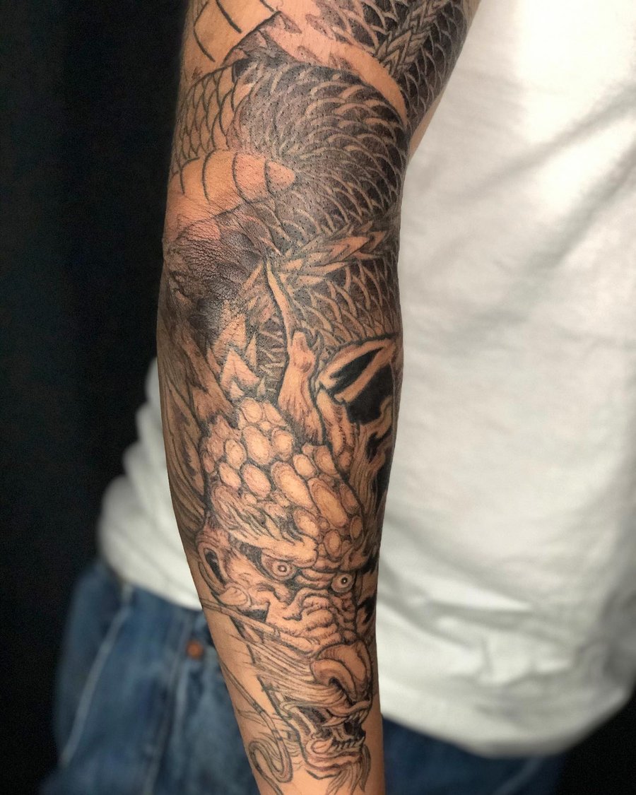 A bold black and grey Japanese dragon tattoo on the arm, featuring intricate scale details and dynamic shading — by Sandra Price, los angeles