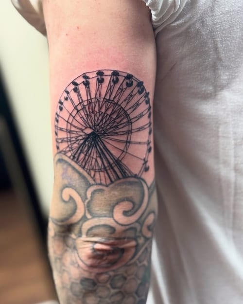 A minimalist black and grey ferris wheel tattoo on the upper arm with clean linework — by Sandra Price, los angeles