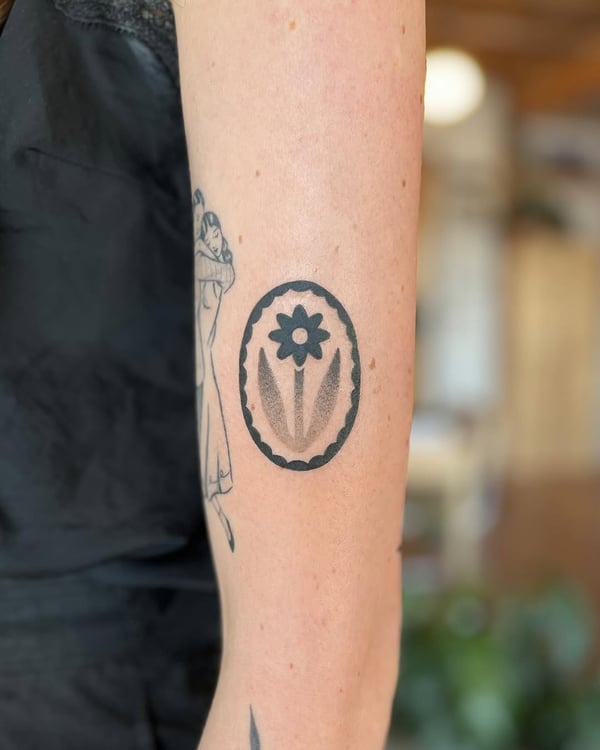 A minimalist black and grey flower tattoo within an oval frame on the forearm — by Dylan Aiello, los angeles