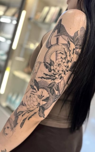 A black and grey tattoo on the upper arm featuring a snake intertwined with large flowers, executed in a Japanese style with detailed linework — by otaybeatdown, los angeles