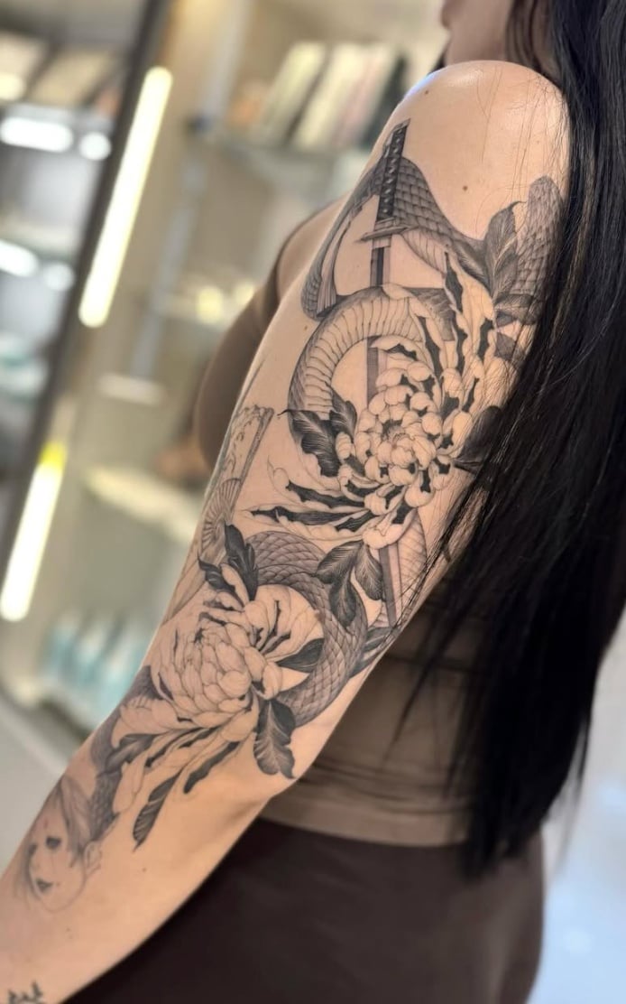 A black and grey tattoo on the upper arm featuring a snake intertwined with large flowers, executed in a Japanese style with detailed linework — by otaybeatdown, los angeles