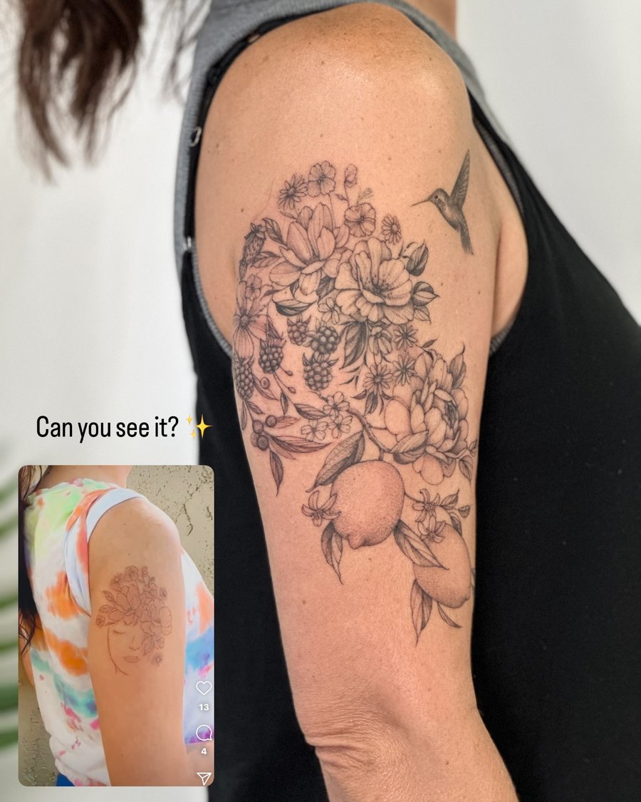 A delicate black and grey floral and fruit bouquet with a hummingbird on the upper arm, featuring fine line details — by Melanie Benoit, los angeles
