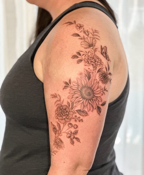 A delicate black and grey floral arrangement tattoo on the upper arm featuring various flowers in fine line style — by Melanie Benoit, los angeles