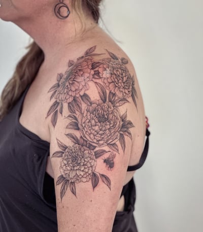 A delicate black and grey tattoo of peony flowers and a bee on the shoulder, featuring intricate floral details — by Melanie Benoit, los angeles