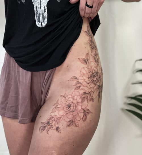 A delicate black and grey floral arrangement tattoo on the thigh, featuring fine line work and botanical details — by Melanie Benoit, los angeles