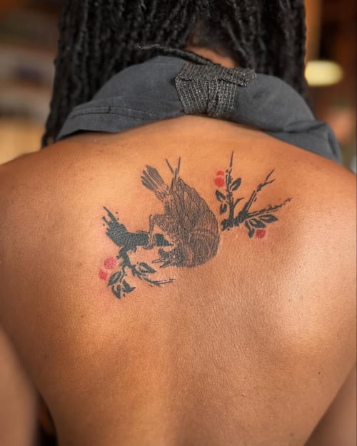 A bold illustrative tattoo of a bird perched on a branch with red accents on the back — by Dylan Aiello, los angeles