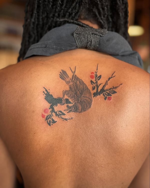 A bold illustrative tattoo of a bird perched on a branch with red accents on the back — by Dylan Aiello, los angeles