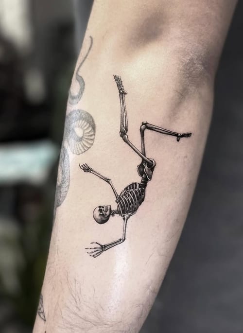 A black and grey fine line tattoo of a skeleton on the forearm, featuring detailed linework and a minimalist style — by Jian Liang, los angeles