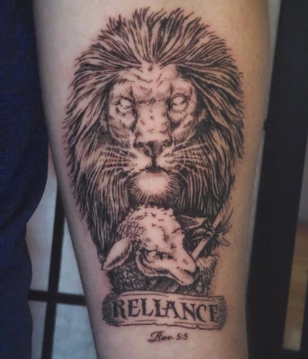 A bold black and grey tattoo of a lion and lamb with script on the forearm, featuring religious symbolism — by Miguel ANGELO, temecula, ca