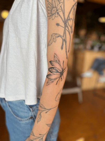A black and grey fine line tattoo of a butterfly and floral elements on the forearm, featuring delicate outlines and shading — by Dylan Aiello, los angeles