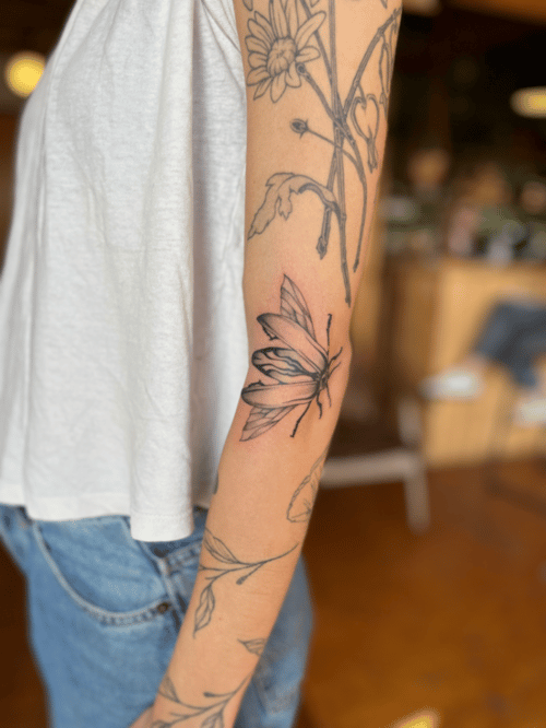 A black and grey fine line tattoo of a butterfly and floral elements on the forearm, featuring delicate outlines and shading — by Dylan Aiello, los angeles