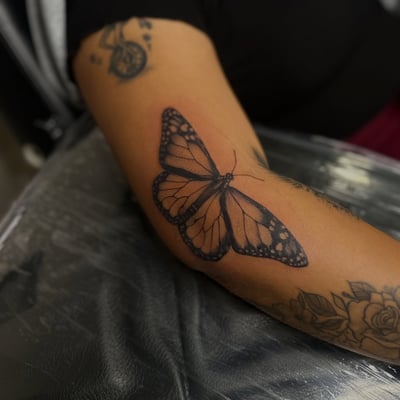 A realistic black and grey monarch butterfly tattoo on the arm — by Maddie Ramirez, los angeles