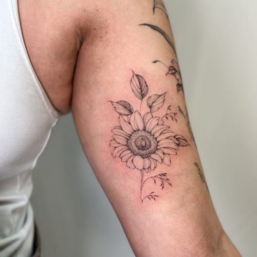 A delicate black and grey fine line sunflower tattoo on the upper arm, showcasing detailed floral elements — by Melanie Benoit, los angeles