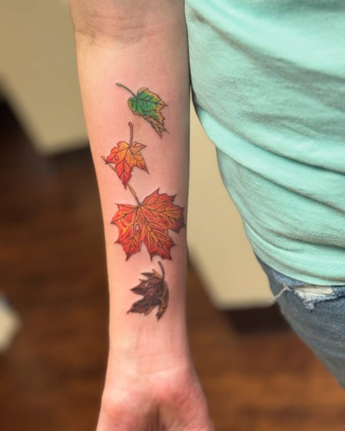 A colorful tattoo of realistic autumn leaves on the forearm, showcasing vibrant fall colors — by Sandra Price, los angeles