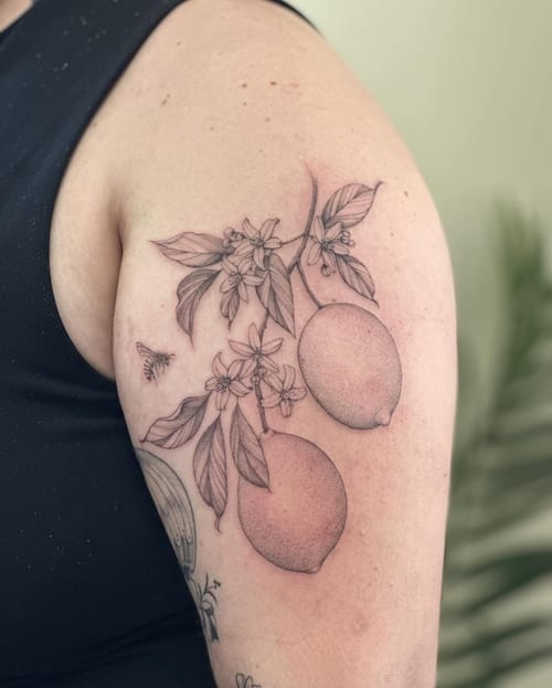 A delicate black and grey tattoo of lemons and flowers on the upper arm, featuring fine line botanical details — by Melanie Benoit, los angeles