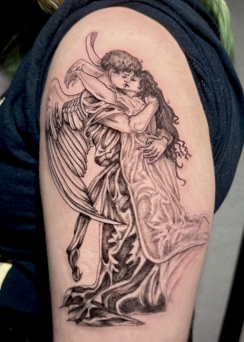 A black and grey tattoo on the upper arm depicting an angel embracing a woman with detailed shading and realistic features — by Shelby Bianco, los angeles