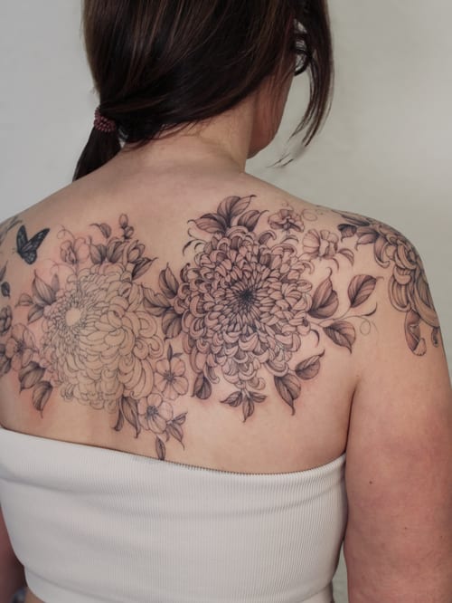 A delicate black and grey floral bouquet tattoo on the back, featuring intricate flower designs with ornate detailing — by Melanie Benoit, los angeles
