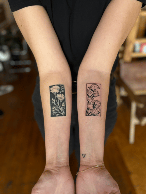 Two black and grey floral tattoos on the forearms, each featuring different flower designs with fine linework and solid black fills — by Dylan Aiello, los angeles