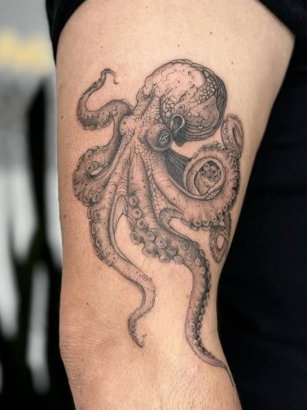 A detailed black and grey tattoo of an octopus on the upper arm, showcasing realistic textures and intricate linework — by otaybeatdown, orange, ca