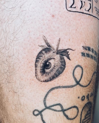 A surreal black and grey tattoo of an eye inside a fruit on the leg, done in an illustrative style — by Level tattoo, los angeles